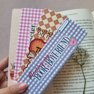 Puede incluir: Tres marcadores de libros con patrones rosa y azul con diseños diferentes. El primer marcador tiene un corazón con una llave y el texto "working on my character". El segundo marcador tiene un corazón con el texto "I love you" y el texto "Meeting my book boyfriend". El tercer marcador tiene un patrón a cuadros y el texto "Do Not Disturb".