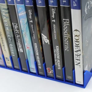 Front view of a blue video game or DVD storage tray in 10 slots featuring wall extensions at the front of each slot to better secure the cases. Ten video games are displayed in the tray.