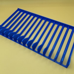 Diagonal right view from above of a blue video game or DVD storage tray in 15 slots featuring wall extensions at the front of each slot to better secure the cases and a slightly elevated back wall. Each slot has a large hole in the base.