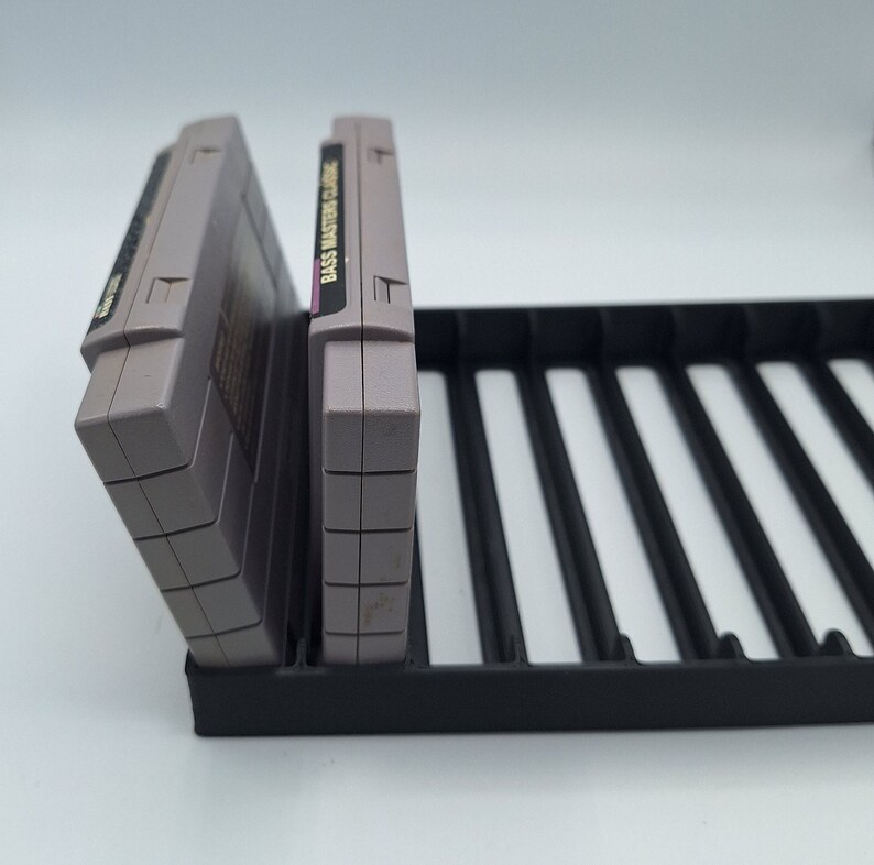 May include: Two gray Super Nintendo game cartridges in a black plastic storage case. The case has multiple slots for storing cartridges.