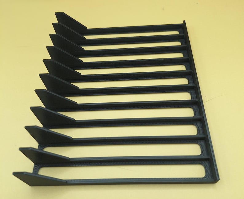 Right side view of a black video game or DVD storage tray in 10 slots featuring wall extensions at the front of each slot to better secure the cases and a slightly elevated back wall. Each slot has a large hole in the base.