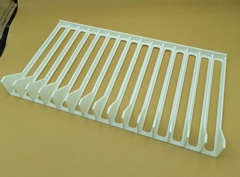 Diagonal right view from above of a white video game or DVD storage tray in 15 slots featuring wall extensions at the front of each slot to better secure the cases and a slightly elevated back wall. Each slot has a large hole in the base.
