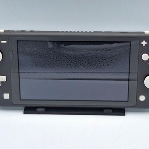 May include: A gray Nintendo Switch Lite handheld gaming console with white buttons. The console is on a black stand.