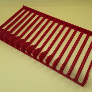 Diagonal right view from above of a red video game or DVD storage tray in 15 slots featuring wall extensions at the front of each slot to better secure the cases and a slightly elevated back wall. Each slot has a large hole in the base.