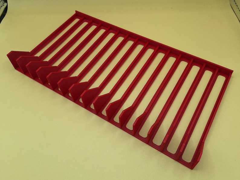 Diagonal right view from above of a red video game or DVD storage tray in 15 slots featuring wall extensions at the front of each slot to better secure the cases and a slightly elevated back wall. Each slot has a large hole in the base.
