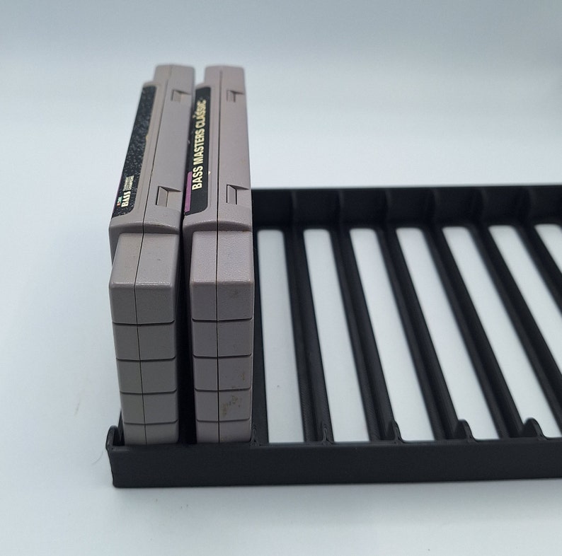 May include: Two gray Super Nintendo game cartridges in a black plastic game cartridge holder. The game cartridges are labeled "Bass Masters Classic".