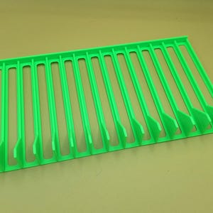 Diagonal right view from above of a bright green video game or DVD storage tray in 15 slots featuring wall extensions at the front of each slot to better secure the cases and a slightly elevated back wall. Each slot has a large hole in the base.