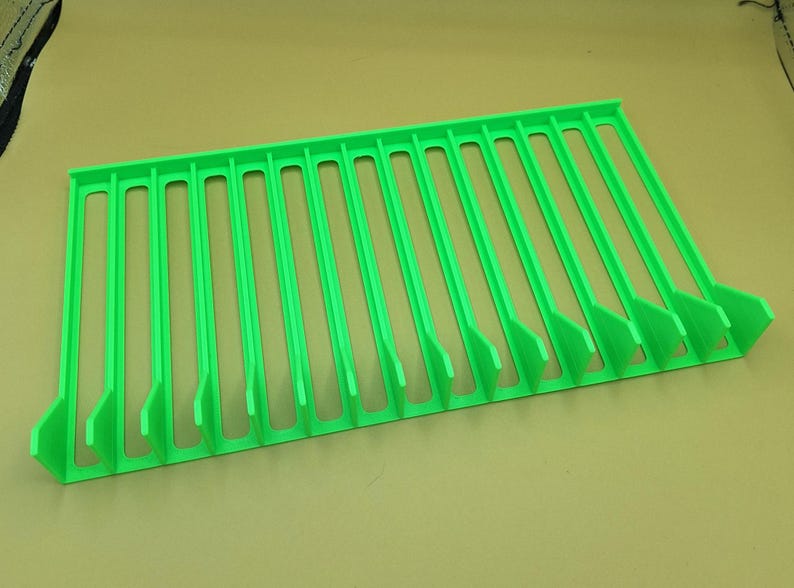 Diagonal right view from above of a bright green video game or DVD storage tray in 15 slots featuring wall extensions at the front of each slot to better secure the cases and a slightly elevated back wall. Each slot has a large hole in the base.