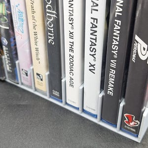 Front view of a gray video game or DVD storage tray in 10 slots featuring wall extensions at the front of each slot to better secure the cases. Ten video games are displayed in the tray.