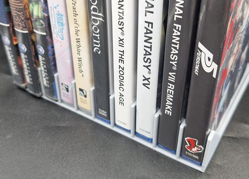 Front view of a gray video game or DVD storage tray in 10 slots featuring wall extensions at the front of each slot to better secure the cases. Ten video games are displayed in the tray.