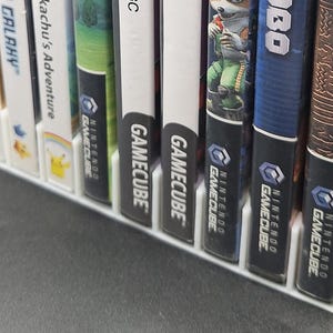 Front view of a white video game or DVD storage tray in 10 slots featuring wall extensions at the front of each slot to better secure the cases. Ten video games are displayed in the tray.