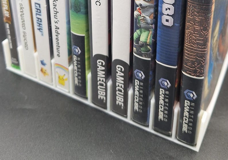 Front view of a white video game or DVD storage tray in 10 slots featuring wall extensions at the front of each slot to better secure the cases. Ten video games are displayed in the tray.