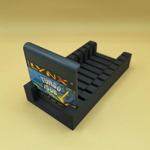 May include: A black plastic game cartridge holder with slots for multiple cartridges. A black Lynx game cartridge with the title "Turbo Sub" is in the holder.