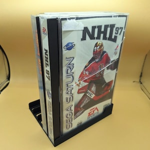 May include: A Sega Saturn video game cartridge case with a black spine and a clear plastic front. The front of the case features a hockey player wearing a red and white jersey with the text "NHL 97" on the top. The game is rated "E" for Everyone by the ESRB.