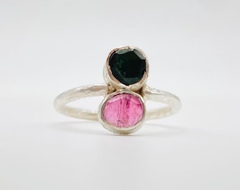 May include: A silver ring featuring two gemstones. The top stone is dark green and the bottom stone is pink.