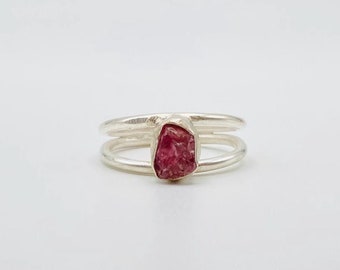 May include: A silver ring with a double band and a pink gemstone.