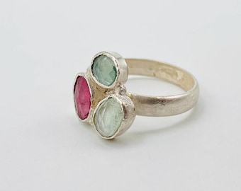 May include: A silver ring set with three gemstones. The ring features two pale blue gemstones and one pink gemstone.