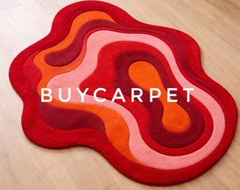May include: A vibrant, abstract rug in shades of red, orange, and pink. The rug features a layered, organic design with the text "BUYCARTPET" in white across the center. The rug is placed on a light-colored wooden floor.