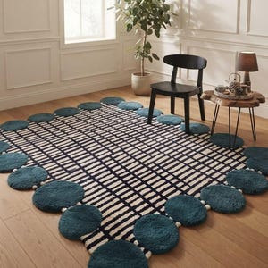 May include: A rectangular area rug featuring a central grid pattern of black and cream lines, bordered by a series of plush, circular teal-colored tufted accents that extend outward from the main rectangular shape along all four edges.