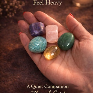 Grief support healing stones set informational cards from AuraBox displayed on a dark warm background with candlelight and dried flowers. The cards explain the meaning of Amethyst, Rose Quartz, Amazonite, Jade and Topaz crystals used for emotional healing, remembrance and comfort during loss. Memorial crystal gift set guide for sympathy, bereavement support and peaceful reflection.