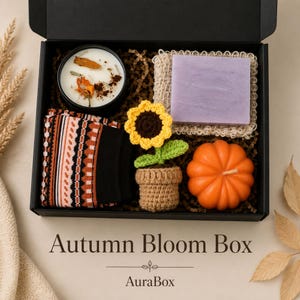 Fall gift box for women featuring a cozy autumn gift basket beautifully arranged in a premium black gift box with pumpkin accent, warm knit socks, sunflower detail, botanical candle, artisan soap and harvest-inspired gifts. Harvest Bliss Box is styled in rich orange, brown, golden yellow and cream fall colors, perfect as a Thanksgiving gift, hostess gift, fall birthday gift, pumpkin care package, autumn gift basket or cozy gift for her.