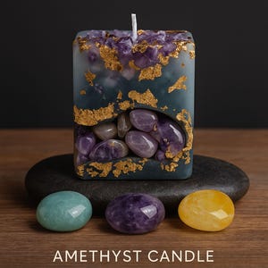 May include: The Golden Aura Signature Set featuring an amethyst candle with gold accents and worry stones. The set includes amazonite, amethyst, and citrine stones. Text on the image reads: Amethyst Candle, Worry Stones, Amazonite, Soothing, Amethyst, Calming, Citrine, Joy.