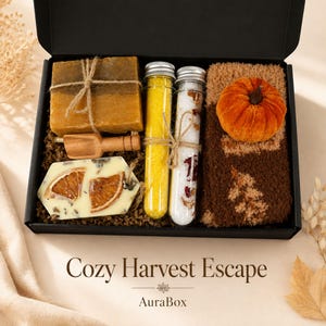 Fall gift box for women featuring a cozy autumn gift basket beautifully arranged in a premium black gift box with pumpkin accent, warm knit socks, sunflower detail, botanical candle, artisan soap and harvest-inspired gifts. Harvest Bliss Box is styled in rich orange, brown, golden yellow and cream fall colors, perfect as a Thanksgiving gift, hostess gift, fall birthday gift, pumpkin care package, autumn gift basket or cozy gift for her.