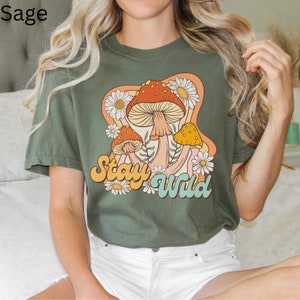 May include: Sage green t-shirt with a graphic of mushrooms and flowers. The text "Stay Wild" is printed in a retro font.