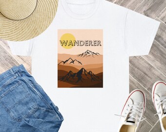Puede incluir: Camiseta blanca con un gráfico de una puesta de sol sobre montañas y la palabra "WANDERER" en texto amarillo.
