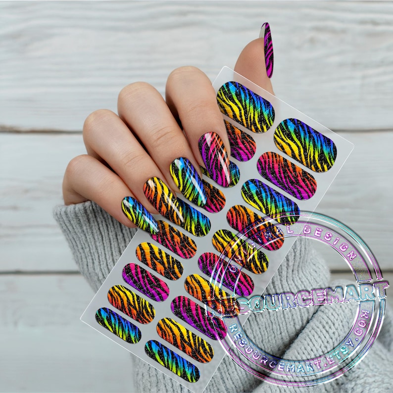 K&ouml;nnte beinhalten: Ein Bogen mit Nagelkunst-Aufklebern mit einem Regenbogen-Zebramuster. Die Aufkleber werden an einer Hand mit passender Nagelkunst gezeigt. Die Nagelkunst-Aufkleber haben ein gl&auml;nzendes Finish und sind in Gelb-, Orange-, Rosa-, Lila- und Blaut&ouml;nen gehalten.