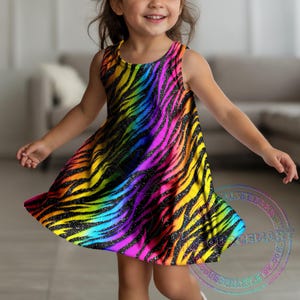 K&ouml;nnte beinhalten: &Auml;rmelloses Kleid mit auff&auml;lligem Regenbogen-Zebramuster. Das Kleid zeigt einen Farbverlauf von Gelb, Orange, Rosa, Lila und Blau mit schwarzen Streifen und Glitzerdetails. Das Kleid ist f&uuml;r Kinder konzipiert.