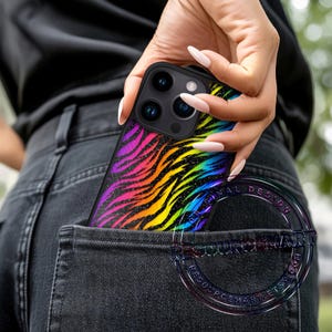K&ouml;nnte beinhalten: Eine schwarze Handyh&uuml;lle mit einem lebendigen Regenbogen-Zebramuster ist teilweise in einer Tasche zu sehen. Die H&uuml;lle hat einen schwarzen Rand und ein glitzerndes Finish, das ein Farbspektrum zeigt.