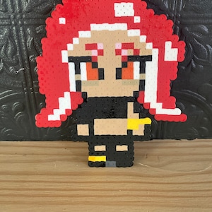 May include: A red-haired, pixelated character with black eyes and a black top. The character is wearing a yellow belt and black boots. The character is made of colorful beads.
