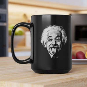 May include: A black coffee mug with a white image of Albert Einstein sticking his tongue out. The mug has a large handle.