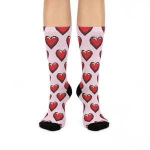 Könnte beinhalten: Ein Paar rosa Socken mit einem roten, pixelartigen Herzmuster.