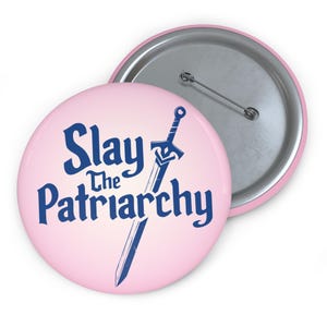 May include: Pink button with a blue sword and the text "Slay the Patriarchy" in a blue, stylized font.