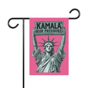 May include: Pink garden flag with a graphic of the Statue of Liberty holding a sign that says "Kamala for President".