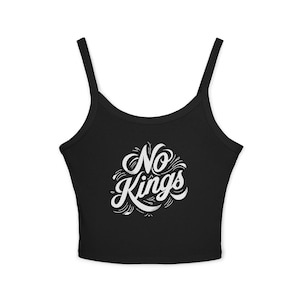 以下が含まれることがあります： 細いストラップが付いた黒のクロップトップ。「No Kings」という白い文字が、装飾的な装飾が施された様式化された筆記体フォントで前面の中央に配置されています。このトップスは柔らかい素材で作られています。