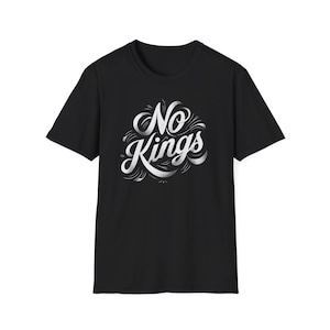 以下が含まれることがあります： 黒いTシャツ。白のスタイリッシュな文字で「No Kings」と書かれています。テキストは装飾的で流れるようなデザインです。Tシャツはクルーネックです。