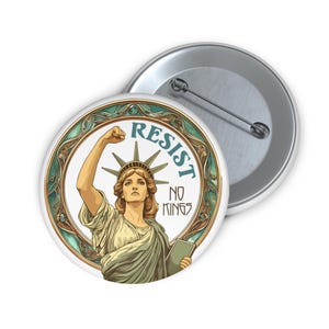 May include: A round button with an illustration of the Statue of Liberty raising her fist. The button has the words "RESIST" and "NO KINGS" in teal. The design is framed by a teal and gold border. A second button is visible in the background.