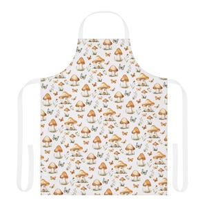 May include: White apron with a repeating pattern of mushroom houses, butterflies, and foliage in brown, orange, and green. The apron has a white neck strap and waist ties. Ideal for cooking or crafting.