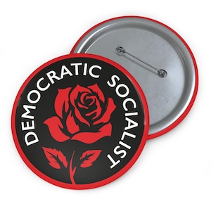 May include: A round button with a red border and a black center. The words "DEMOCRATIC SOCIALIST" are in white around the edge. A red rose is in the center. A second button is visible behind the first.