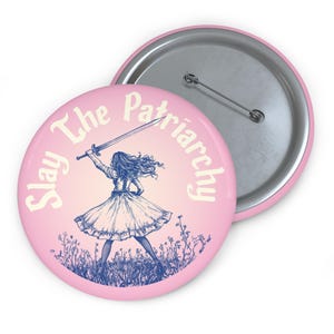 May include: A pink button with a white outline and the text "Slay The Patriarchy" in a white font. A blue illustration of a woman holding a sword is in the center of the button.