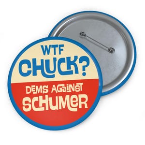 May include: A round button with a blue border and a silver pin back. The button features the text "WTF CHUCK?" in blue, above "DEMS AGAINST SCHUMER" in red and white.