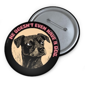 May include: A black and white button with a black dog illustration and the text "He doesn't even have a dog." in pink.