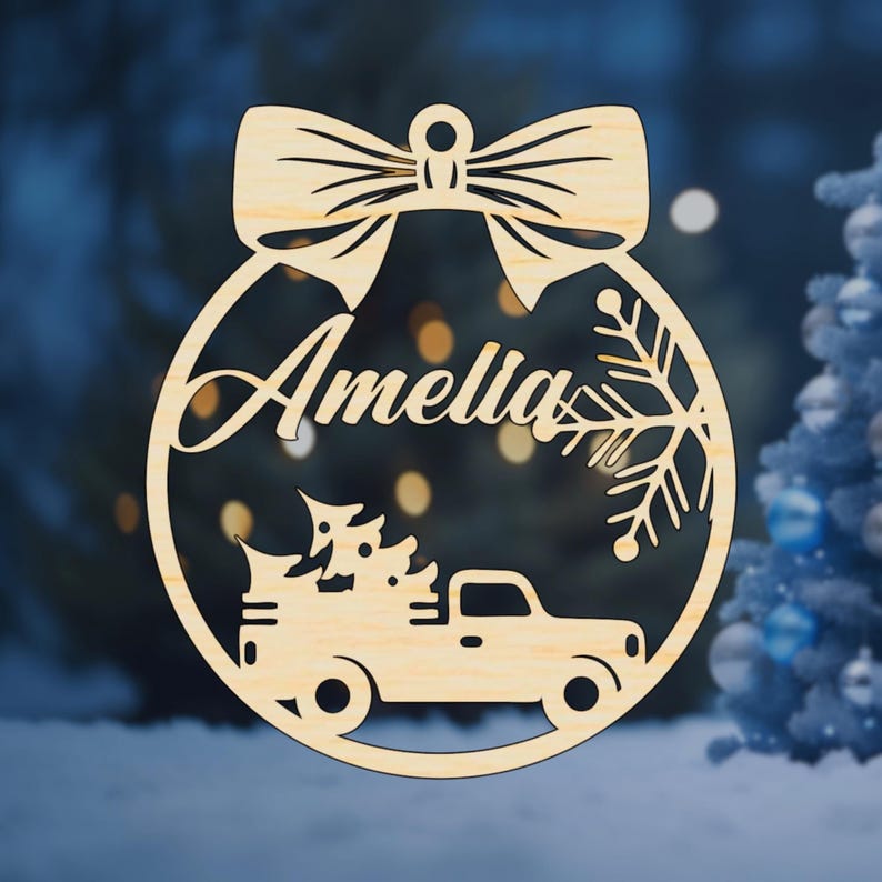 K&ouml;nnte beinhalten: Ein runder Weihnachtsbaumschmuck aus Holz mit einer Schleife oben. Der Anh&auml;nger zeigt einen LKW, der einen Weihnachtsbaum transportiert, einen Schneeflock und den Namen "Amelia" darauf.