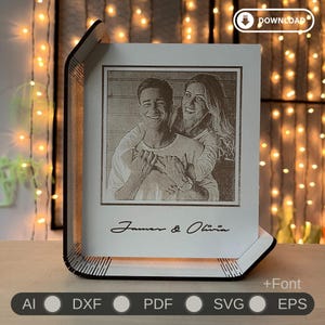 Può includere: Una cornice in legno con un'immagine incisa al laser di una coppia, con i nomi "James & Olivia" in basso. La cornice ha una luce integrata e un pulsante di download in alto a destra. La cornice è circondata da luci a stringa.