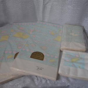 May include: Several packages of vintage baby-themed paper napkins. The napkins have a light blue background with a repeating pattern of yellow, pink, and white illustrations. Some packages are sealed in clear plastic.