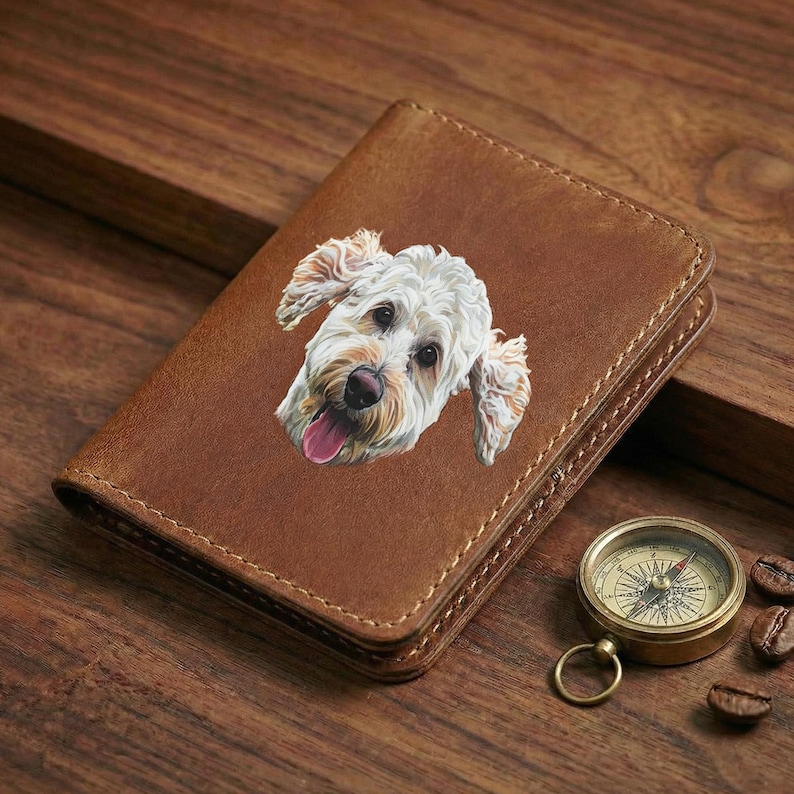 May include: A brown leather wallet featuring a detailed illustration of a white and tan dog with its tongue out. A small brass compass and coffee beans are next to the wallet. The wallet has a stitched border.