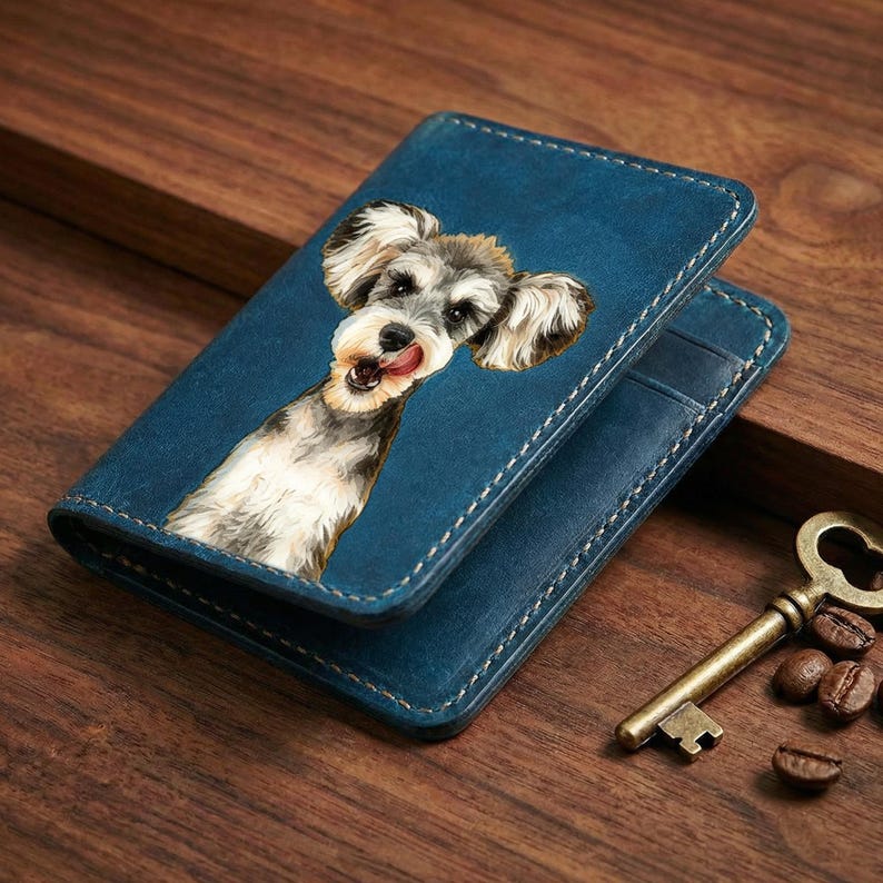 May include: Blue leather wallet featuring a Schnauzer dog portrait. The wallet has white stitching and a bi-fold design. A vintage key and coffee beans are next to the wallet on a wooden surface.